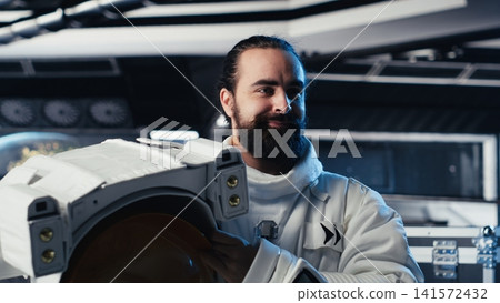 Portrait of smiling astronaut holding helmet inside space station, preparing for planetary mission outside. Happy starship crew member beginning landing procedures on solar system planet Portrait of smiling astronaut holding helmet inside space station, preparing for planetary mission outside. Happy starship crew member beginning landing procedures on solar system planet 141572432