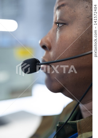Close up of military operator speaking through headset microphone while monitoring control room. Female army dispatcher relays mission updates to personnel from command center Close up of military operator speaking through headset microphone while monitoring control room. Female army dispatcher relays mission updates to personnel from command center 141572484