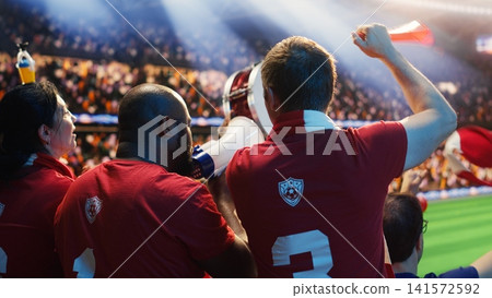 Ecstatic friends celebrate match victory in soccer stadium stands. Back view of delighted football supporters hugging after positive result in live sports arena Ecstatic friends celebrate match victory in soccer stadium stands. Back view of delighted football supporters hugging after positive result in live sports arena 141572592