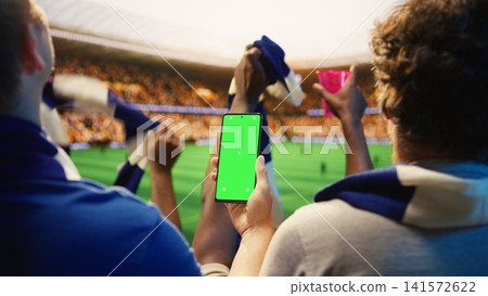 Close up of mockup phone used by fan in stadium to compare odds during soccer match day. Football supporter checking predictions on live score app on green screen smartphone Close up of mockup phone used by fan in stadium to compare odds during soccer match day. Football supporter checking predictions on live score app on green screen smartphone 141572622