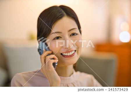 A woman in her 40s relaxing in her room at night and looking at her smartphone. A woman in her 40s relaxing in her room at night and looking at her smartphone. 141573429