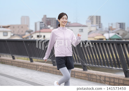 A middle-aged woman walking along the riverbank in sportswear. 141573450