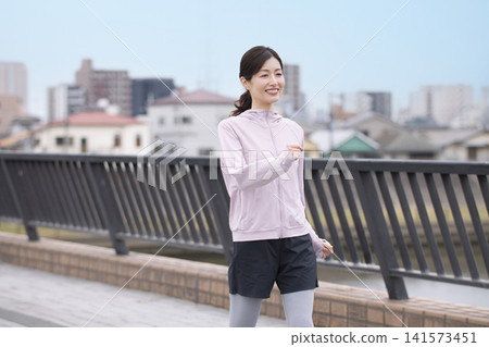 A middle-aged woman walking along the riverbank in sportswear. A middle-aged woman walking along the riverbank in sportswear. 141573451