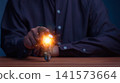 Businessman touching a glowing light bulb with sparks. This concept represents a bright business idea, innovation, technology, creativity, inspiration, and future success. 141573664