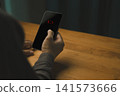 Person holding a smartphone with a red low battery warning icon on a black screen. Represents modern technology, power loss, and mobile connection anxiety in daily life. 141573666