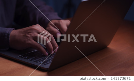 Close up of male hands typing on a laptop computer keyboard at night. Working late on modern business technology, internet connection, remote work, and online digital network communication. Close up of male hands typing on a laptop computer keyboard at night. Working late on modern business technology, internet connection, remote work, and online digital network communication. 141573671
