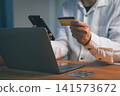 Man engages in online shopping and e-commerce, using a credit card for payment. He accesses mobile banking on a smartphone and internet via laptop for this finance transaction. 141573672