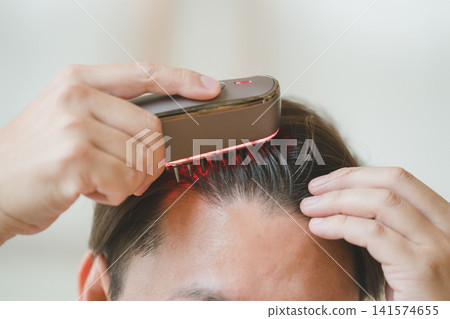 Close-up of a man's head as he applies an electric brush to his forehead with both hands. Close-up of a man's head as he applies an electric brush to his forehead with both hands. 141574655