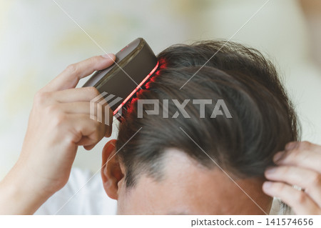 Close-up of a man's head as he uses an electric brush to care for his ears. Close-up of a man's head as he uses an electric brush to care for his ears. 141574656