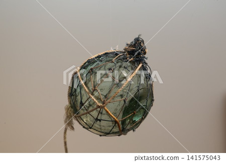Close-up of a glass float wrapped in a fishing net. Close-up of a glass float wrapped in a fishing net. 141575043