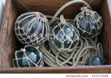 Glass floats and rope in a wooden box Glass floats and rope in a wooden box 141575098