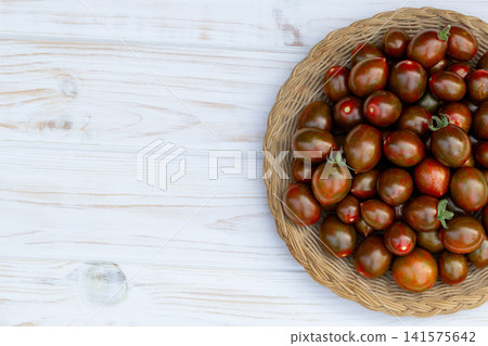 Dark cherry tomatoes in the woven plate on the white table. Dark cherry tomatoes in the woven plate on the white table. 141575642