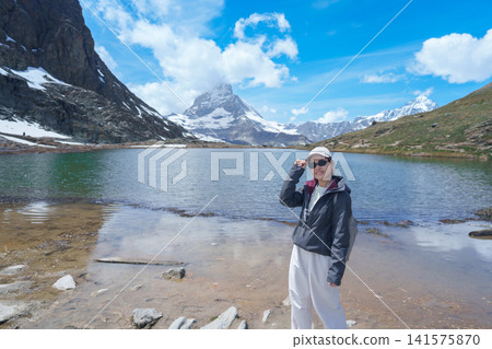 Woman Tourist Exploring Zermatt, Switzerland. happy hiker sightseeing iconic Matterhorn Swiss Alps at Riffelsee Lake, Famous European Landmark, Hiking Attraction and Travel Destination in Europe 141575870