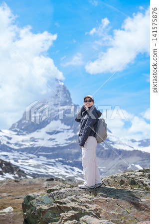 Woman Tourist Exploring Zermatt, Switzerland in summer. Happy Hiker Standing on Rock along Hiking Trail with Matterhorn, Swiss Alps, Famous Europe Landmark, Hiking Attraction and Travel Destination Woman Tourist Exploring Zermatt, Switzerland in summer. Happy Hiker Standing on Rock along Hiking Trail with Matterhorn, Swiss Alps, Famous Europe Landmark, Hiking Attraction and Travel Destination 141575876