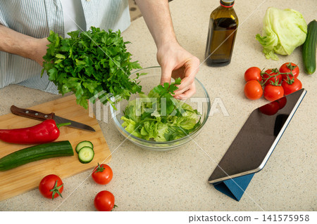 Cooking. Hands prepare fresh salad using tablet for recipe guidance Cooking. Hands prepare fresh salad using tablet for recipe guidance 141575958