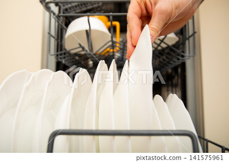 Dishwasher. Hand carefully removes clean plates from dishwasher in kitchen Dishwasher. Hand carefully removes clean plates from dishwasher in kitchen 141575961