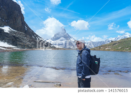 man Tourist Exploring Zermatt, Switzerland. happy hiker sightseeing iconic Matterhorn Swiss Alps at Riffelsee Lake, Famous European Landmark, Hiking Attraction and Travel Destination in Europe man Tourist Exploring Zermatt, Switzerland. happy hiker sightseeing iconic Matterhorn Swiss Alps at Riffelsee Lake, Famous European Landmark, Hiking Attraction and Travel Destination in Europe 141576015