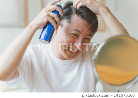 A man in his 40s smiles as he sprays hairspray onto his scalp. A man in his 40s smiles as he sprays hairspray onto his scalp. 141576166