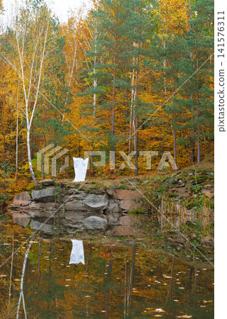 Playful ghost halloween costume White fabric drapes over the figure, while glasses and cap add personality charm. Colorful fall foliage tree trunks fallen leaves and natural woodland surroundings Playful ghost halloween costume White fabric drapes over the figure, while glasses and cap add personality charm. Colorful fall foliage tree trunks fallen leaves and natural woodland surroundings 141576311