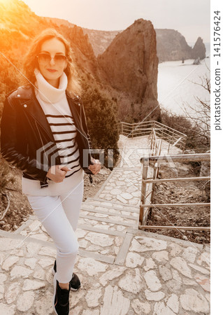 Woman cliffside travel walking down stone stairs wearing a leather jacket and striped sweater overlooking a scenic coastal view Woman cliffside travel walking down stone stairs wearing a leather jacket and striped sweater overlooking a scenic coastal view 141576424