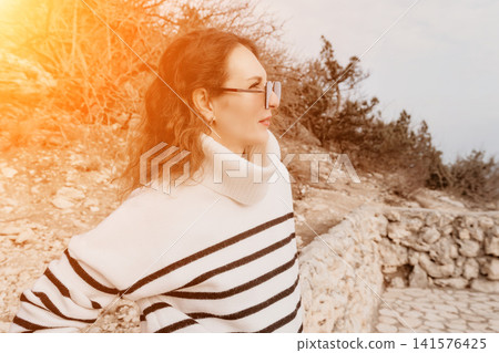 Woman Sweater Landscape Elegant woman in striped sweater and glasses gazes at a rugged landscape from a stone path. Woman Sweater Landscape Elegant woman in striped sweater and glasses gazes at a rugged landscape from a stone path. 141576425