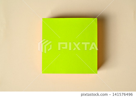 Flat lay of a blank bright green square sticky note block centered on a warm beige background with copy space 141576496