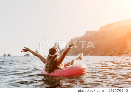 Woman, floating, sea. Young woman relaxing on inflatable ring in open sea near rocky coast, enjoying summer vacation. Woman, floating, sea. Young woman relaxing on inflatable ring in open sea near rocky coast, enjoying summer vacation. 141576540