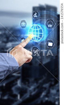 Hand of a businessman touching a futuristic virtual interface with a global network globe icon and technology icons, with a blurred modern city in the background. Concept of Remote working 141576554