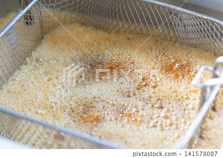Closeup of food frying hot oil inside commercial deep fryer bubbling oil highlighting cooking process crispy texture professional kitchen preparation 141578087