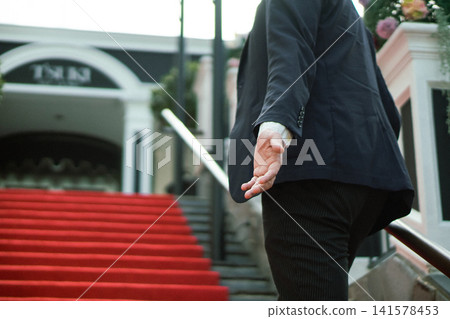 A man reaches out to take his girlfriend's hand on the stairs of a red carpet. (Similar to matchmaking, dating, The Bachelor, and reality dating shows.) 141578453