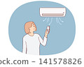 Woman stands under air conditioner and uses remote control to switch temperature mode 141578826