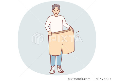 Lost weight man with big shorts in hands is surprised at size of own clothes from past Lost weight man with big shorts in hands is surprised at size of own clothes from past 141578827