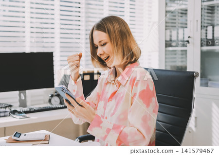 Confident and Composed: A professional businesswoman exudes confidence and composure as she works on her laptop, surrounded by the vibrant energy of a modern office space. Confident and Composed: A professional businesswoman exudes confidence and composure as she works on her laptop, surrounded by the vibrant energy of a modern office space. 141579467
