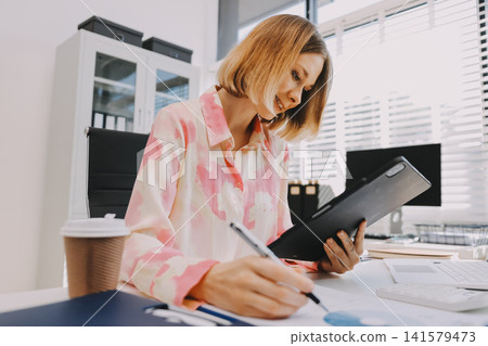Young businesswoman smiling as she works on a laptop sitting in an modern office Young businesswoman smiling as she works on a laptop sitting in an modern office 141579473