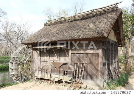 An old farmhouse with a thatched roof and a waterwheel 141579627