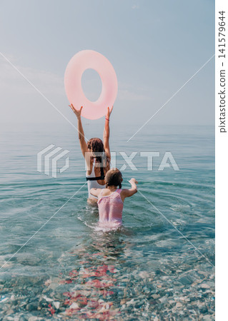 Sea vacation family enjoying a swim in the clear ocean water with a pink inflatable ring during summer holidays Sea vacation family enjoying a swim in the clear ocean water with a pink inflatable ring during summer holidays 141579644