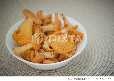 Raw chanterelle mushrooms in white bowl on round woven placemat. Raw chanterelle mushrooms in white bowl on round woven placemat. 141582466