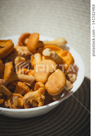 Raw yellow chanterelle mushrooms in white bowl on woven mat background. Raw yellow chanterelle mushrooms in white bowl on woven mat background. 141582468