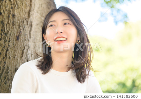 Japanese woman relaxing while leaning against a tree Japanese woman relaxing while leaning against a tree 141582600