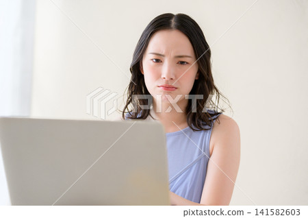 一位日本女性一邊看著筆記型電腦一邊沉思。 一位日本女性一邊看著筆記型電腦一邊沉思。 141582603