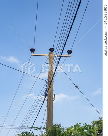 Concrete electricity pole with ceramic insulators and multiple crossing power lines against a blue sky in a tropical setting Concrete electricity pole with ceramic insulators and multiple crossing power lines against a blue sky in a tropical setting 141582903
