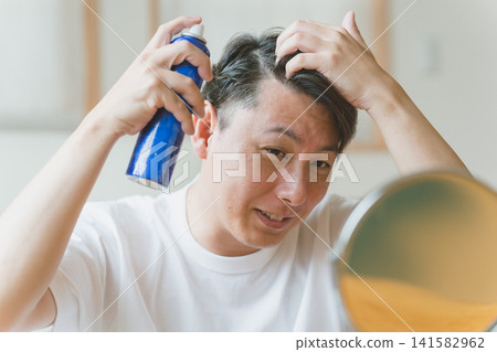一位四十多歲的男子一邊往頭皮上噴髮膠，一邊露出笑容。 141582962