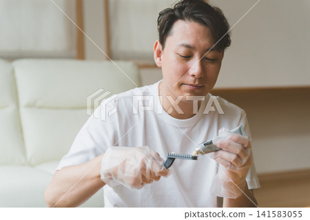 A man in his 40s wearing plastic gloves dispenses cream onto a brush. A man in his 40s wearing plastic gloves dispenses cream onto a brush. 141583055