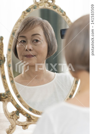一位老婦人在鏡子前整理頭髮。 141583509