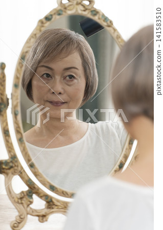 一位老婦人在鏡子前整理頭髮。 一位老婦人在鏡子前整理頭髮。 141583510
