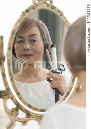 一位老婦人在鏡子前整理頭髮。 一位老婦人在鏡子前整理頭髮。 141583516