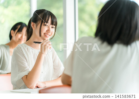 Elementary and junior high school students (friends) talking to the student in front of them during class at school Elementary and junior high school students (friends) talking to the student in front of them during class at school 141583671