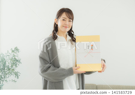 A woman handing over a gift with a decorative paper wrapping. A woman handing over a gift with a decorative paper wrapping. 141583729