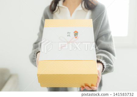 一位女士遞上一份用精美包裝紙包裹的禮物。 一位女士遞上一份用精美包裝紙包裹的禮物。 141583732