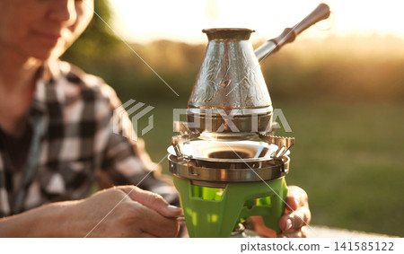 Woman Making Coffee In A Cezve On A Portable Camping Stove Boils Water Woman Making Coffee In A Cezve On A Portable Camping Stove Boils Water 141585122